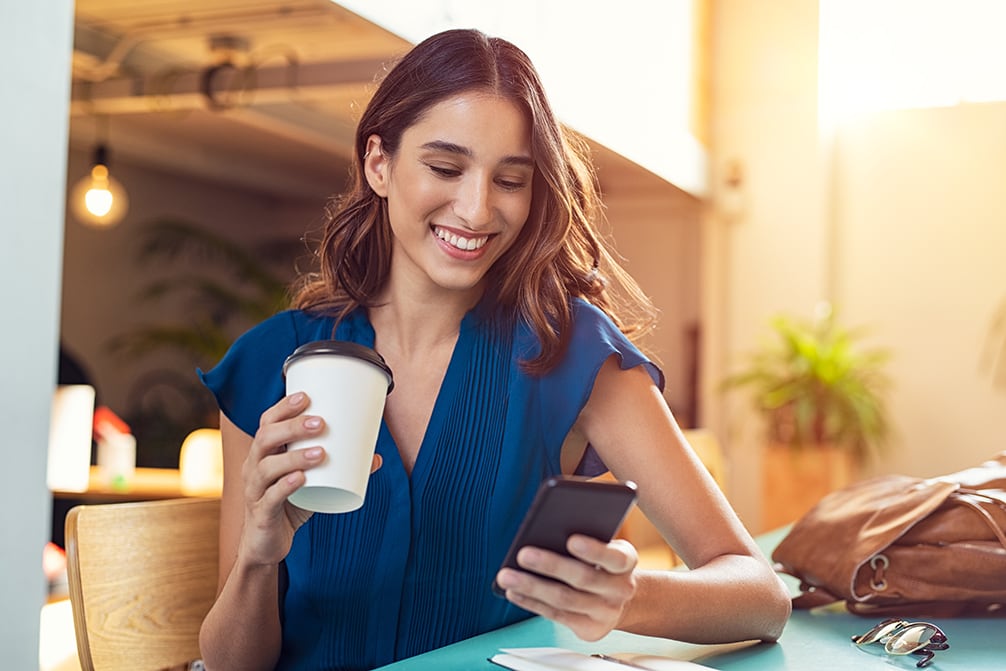 woman holding coffee paper cup and looking at smartphone